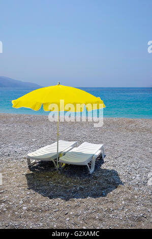 Gelbe Sonnenschirm und zwei weiße Liegestühle am Strand Stockfoto