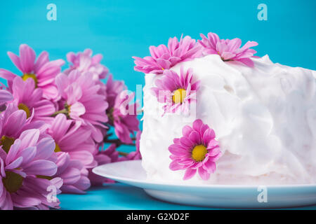 Weiße cremige Kuchen mit Blumen auf dem blauen Hintergrund aus Holz. Geringe Schärfentiefe. Stockfoto