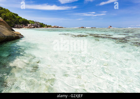 Kristallklares Wasser in der Nähe von Source d ' Argent in La Digue, Seychellen mit blauem Himmel Stockfoto