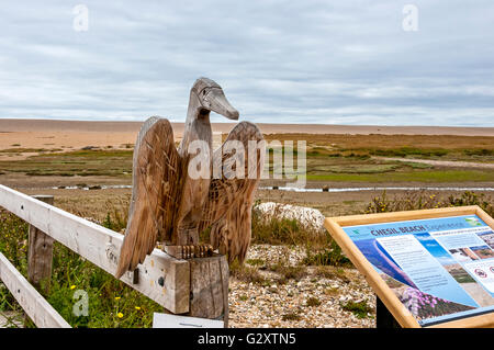 Ein Holzsteg, verziert mit Schnitzereien der lokalen Fauna kreuzt eine Wildlife-reiche Gezeiten-Lagune an eine breite Bank glatte Kieselsteine Stockfoto