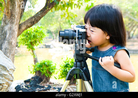 Zwei Jahre altes kleines Mädchen nehmen Foto mit Spiegelreflexkamera auf Stativ im Freien in einem Park. Kind viel Spaß beim üben Stockfoto