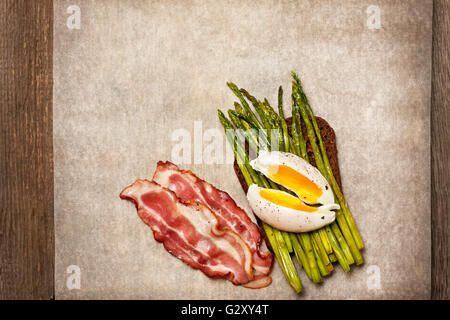 Toast mit gebackenem Spargel, gekochtem Ei, Speck auf Papier (Draufsicht) Stockfoto