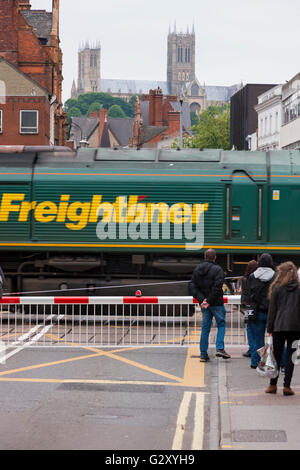 Menschen / Fußgänger warten auf eine Eisenbahn Bahnübergang Barriere in Lincoln, Lincolnshire, UK, während ein Güterzug durchläuft. Stockfoto