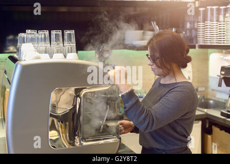Weibliche Barista oder Kellnerin mache eine Tasse Cappuccino in einem Kaffeehaus oder in der Cafeteria der heiße aufgeschäumte Milch in den Kaffee gießen Stockfoto