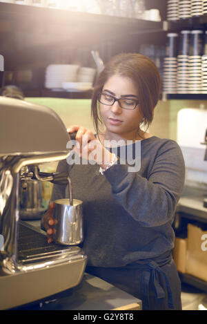 Weibliche Barista oder Kellnerin mache eine Tasse Cappuccino in einem Kaffeehaus oder in der Cafeteria der heiße aufgeschäumte Milch in den Kaffee gießen Stockfoto