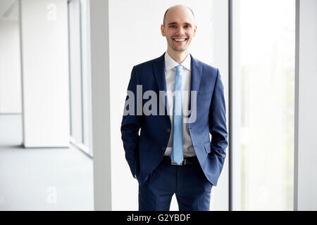 Porträt von fröhlichen jungen Geschäftsmann im Büro stehen. Hellen Hintergrund. Hände in den Taschen. Stockfoto