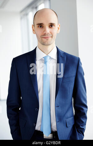 Ruhig junger Geschäftsmann im Büro stehen. Hände in den Taschen. Hellen Hintergrund. Stockfoto