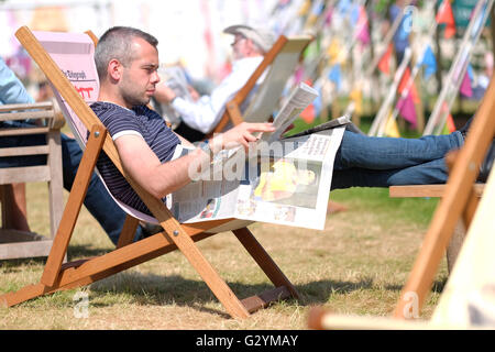 Hay Festival 2016, Wales, UK - Juni 2016 - ein Mann legt seine Füße und liest seine Zeitung im hellen Schein der Morgensonne mit Temperaturen bis zu 22 ° c heute. Stockfoto