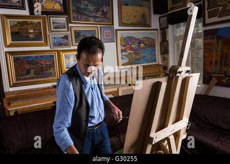 Kontemplative männlichen Maler vor seiner Staffelei mit Pinsel in einem Studio mit original-Kunstwerke an der Wand hängen. Stockfoto