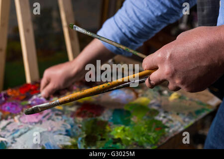 Pinsel in der Hand des Künstlers unter bunten Palette von blended Ölfarben in einer Galerie hautnah Stockfoto