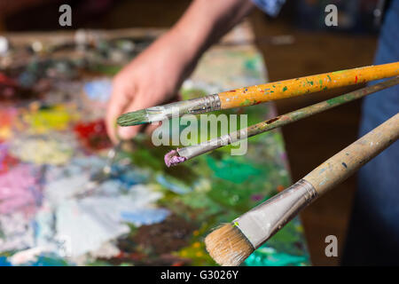 Nahaufnahme der Pinsel in der Hand eines Malers unter bunten Palette im agallery Stockfoto