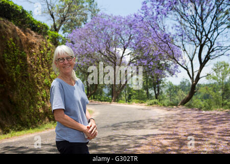 Sri Lanka, Ella, senior Frau Tourist auf Landstraße unter blühende Jacaranda-Bäume Stockfoto