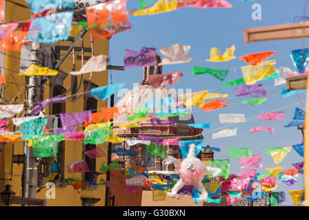 Festliche Papel Picado Banner schmücken eine Straße mit Blick auf die Kuppel des Oratorio de San Felipe Neri Kirche im historischen Zentrum von San Miguel de Allende, Mexiko. Stockfoto