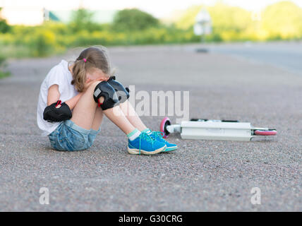 Kleine Mädchen fiel von der Roller auf der Straße. Stockfoto