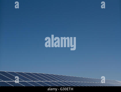 Eine lange Reihe von Solarpaneelen erzeugt sauberen, erneuerbaren Strom unter einem klaren, blauen Himmel mit viel Kopierraum darüber. Stockfoto