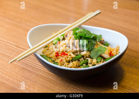 Asiatische Riсe mit Meeresfrüchten und Gemüse in ovalen Platte mit Bambus-sticks auf einem Holztisch im asiatischen restaurant Stockfoto