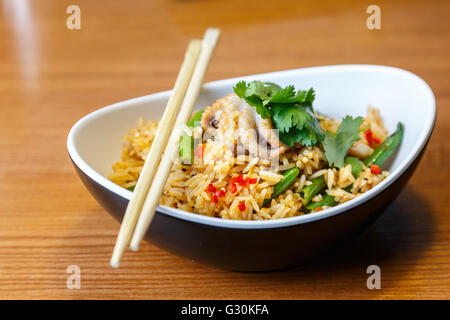 Asiatische Riсe mit Meeresfrüchten und Gemüse in ovalen Platte mit Bambus-sticks auf einem Holztisch im asiatischen restaurant Stockfoto