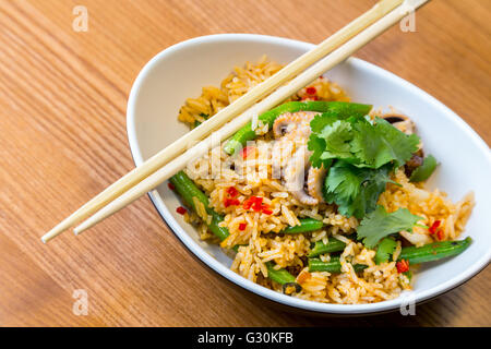 Asiatische Riсe mit Meeresfrüchten und Gemüse in ovalen Platte mit Bambus-sticks auf einem Holztisch im asiatischen restaurant Stockfoto