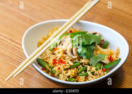 Asiatische Riсe mit Meeresfrüchten und Gemüse in ovalen Platte mit Bambus-sticks auf einem Holztisch im asiatischen restaurant Stockfoto