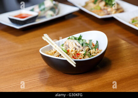 Asiatische Riсe mit Meeresfrüchten und Gemüse in ovalen Platte mit Bambus-sticks auf einem Holztisch im asiatischen restaurant Stockfoto