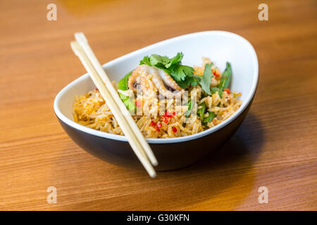 Asiatische Riсe mit Meeresfrüchten und Gemüse in ovalen Platte mit Bambus-sticks auf einem Holztisch im asiatischen restaurant Stockfoto