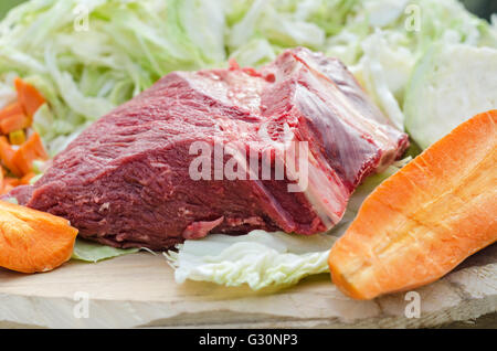 Ein großes Stück rohes Rindfleisch und Gemüse auf einem rauen Brett Zutaten zum Kochen beim Picknick Stockfoto