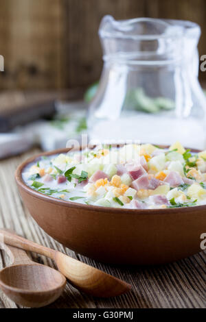 Traditionelle russische Sommer kalte Suppe Okroschka mit Kefir in Keramikschale auf rustikalen Holztisch, Zutaten Stockfoto