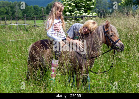 Kleines Mädchen reitet Pony, Mädchen zu Pferd und Frau auf einer Wiese, Kind auf Shetland Pony Stockfoto