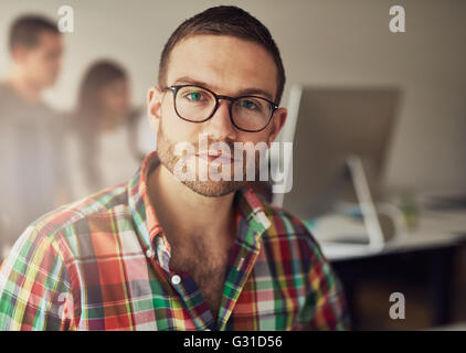 Nahaufnahme eines schönen bärtigen Arbeiter tragen von Brillen und Flanellhemd im kleinen Büro mit anderen Mitarbeitern im Hintergrund Stockfoto