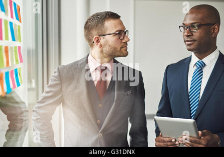 Zwei stilvolle multirassische Führungskräften in eine ernsthafte Diskussion stand vor einem hellen Fenster mit flare Stockfoto