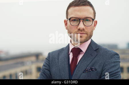 Schweren intensiven junger Geschäftsmann mit Brille stehen im Freien auf einer Open-Air-Balkon, starrte auf die Kamera, Kopf und Schulter Stockfoto