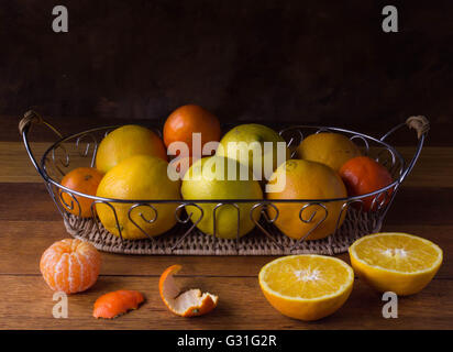 Stillleben, bestehend aus orange, Zitrone und Mandarine Zitrusfrüchte im Metallkorb auf rustikalen Holztisch Stockfoto