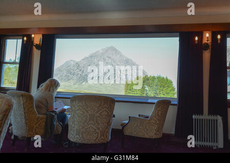 Frau sitzt vor einem atemberaubenden Blick auf Buchaille Etive Mor aus dem Fenster des Kings House Hotel, Glencoe, Schottland, Vereinigtes Königreich Stockfoto