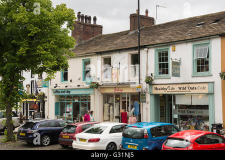 Menschen passieren unabhängige Läden, Cafés und parkende Autos auf der High Street von der historischen Marktstadt von Skipton, North Yorkshire, England. Stockfoto