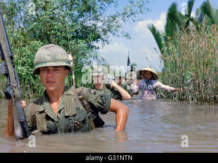 US-Armee Soldaten PFC Fred Greenleaf, mit C Company, 3. Bataillon, 7. Infanterie-Division, 199. Light Infantry Brigade, überquert eine tiefe Bewässerungskanal zusammen mit Mitgliedern der 5. ARVN Ranger Gruppe auf dem Weg zu einem Vietcong kontrollierten Dorf während des Betriebs klingelte Dong 21. November 1967 in Cat Lai, Südvietnam. Stockfoto