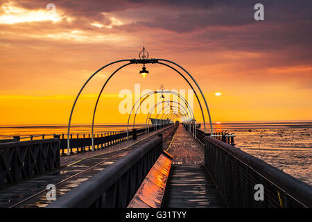 Southport, Merseyside, England.   Großbritannien Wetter. 5. Juni 2016.  Dunkle Gewitterwolken über der veteran Pier Struktur nach Regenschauer, kühlt die Luft, kurz vor dem Sonnenuntergang am späten Abend.  Die tief rote Kugel der untergehenden Sonne richtet sich fast mit der Reflexion mit der Tram, die Linien schafft eine Illusion eines Resorts bis unendlich irgendwo heraus über die irische Seeküste und die Rötung des nassen Strand Sand Reise. Bildnachweis: MediaWorldImages/Alamy Live-Nachrichten Stockfoto