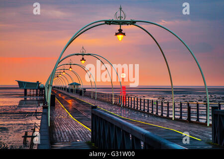 Southport, Merseyside, England.   Großbritannien Wetter. 5. Juni 2016.  Dunkle Gewitterwolken über der veteran Pier Struktur nach Regenschauer, kühlt die Luft, kurz vor dem Sonnenuntergang am späten Abend.  Die tief rote Kugel der untergehenden Sonne richtet sich fast mit der Reflexion mit der Tram, die Linien schafft eine Illusion eines Resorts bis unendlich irgendwo heraus über die irische Seeküste und die Rötung des nassen Strand Sand Reise. Bildnachweis: MediaWorldImages/Alamy Live-Nachrichten Stockfoto