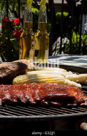 Gegrillte Schweinerippchen mit Baby-Back, Mais und gebackenen Kartoffeln gekocht außerhalb auf einem Holzkohlegrill in einem Garten Stockfoto