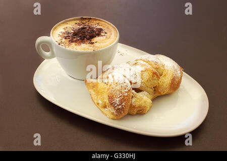 Italienische cremig heißen Cappuccino mit Schokoladenpulver mit Sahne Butter Brioche auf dem Tisch, bereit für das Frühstück Stockfoto