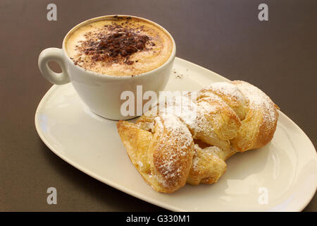 Italienische cremig heißen Cappuccino mit Schokoladenpulver mit Sahne Butter Brioche auf dem Tisch, bereit für das Frühstück Stockfoto