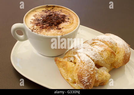 Italienische cremig heißen Cappuccino mit Schokoladenpulver mit Sahne Butter Brioche auf dem Tisch, bereit für das Frühstück Stockfoto