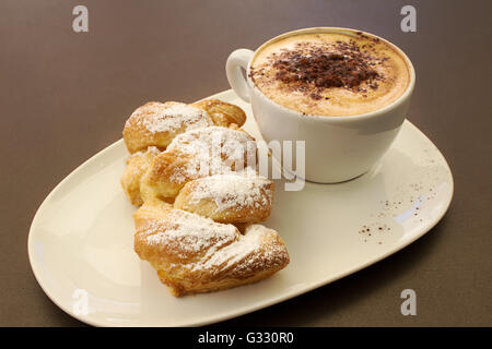 Italienische cremig heißen Cappuccino mit Schokoladenpulver mit Sahne Butter Brioche auf dem Tisch, bereit für das Frühstück Stockfoto