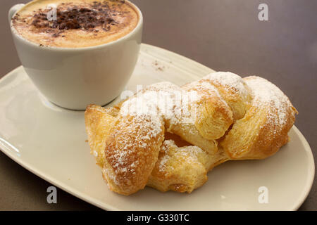 Italienische cremig heißen Cappuccino mit Schokoladenpulver mit Sahne Butter Brioche auf dem Tisch, bereit für das Frühstück Stockfoto