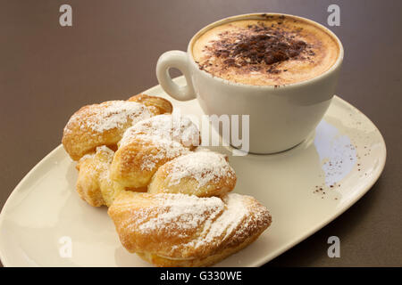 Italienische cremig heißen Cappuccino mit Schokoladenpulver mit Sahne Butter Brioche auf dem Tisch, bereit für das Frühstück Stockfoto