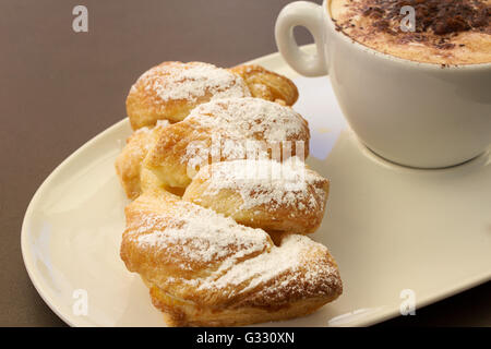 Italienische cremig heißen Cappuccino mit Schokoladenpulver mit Sahne Butter Brioche auf dem Tisch, bereit für das Frühstück Stockfoto