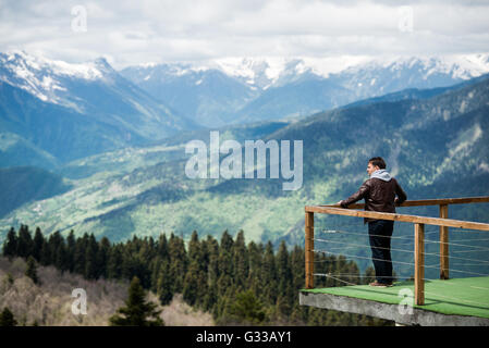 Junger Mann in Haube Blick auf die Berglandschaft von hölzernen Pier am Morgen. Hintere Ansicht Foto Stockfoto