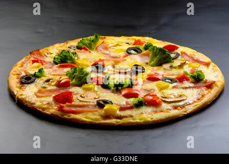 Pizza auf einem dunklen Hintergrund mit Schinken, Champignons, Blumenkohl, Oliven, Käse und Paprika Stockfoto