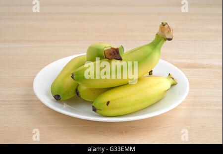 Einem weißen Teller mit kleinen Bananen auf einem Holztisch. Stockfoto