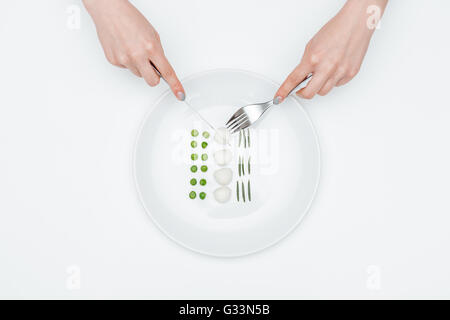 Draufsicht der Hände der jungen Frau Essen, grüne Erbsen, Mozzarella und Kräutern mit Messer und Gabel auf weißem Hintergrund Stockfoto