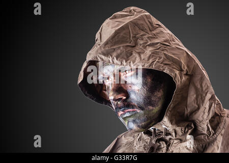 ein Soldat trägt einen Poncho oder Regenmantel und Armee Camouflage Gesicht malen Stockfoto